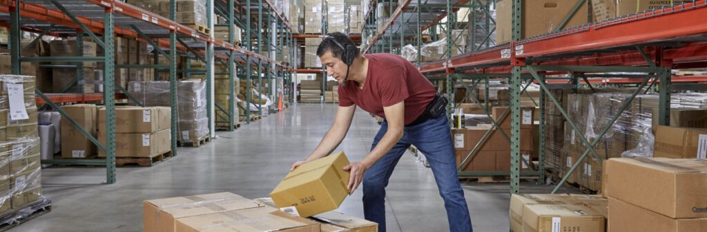A worker in a warehouse using a voice-directed headset while moving packages