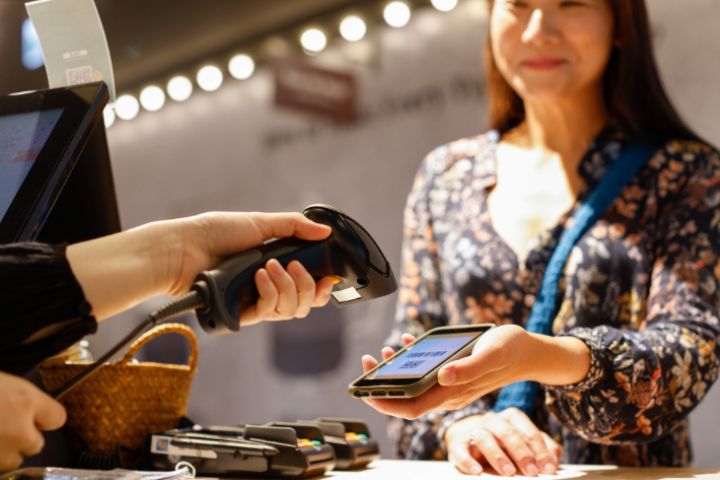 A retail worker using a handheld barcode scanner on a customer's phone